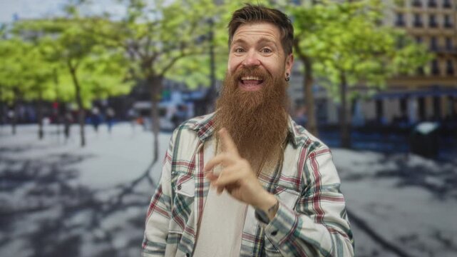 Bearded man smiling and making call gesture with hand on busy city street amid pedestrians; friendly connection bonding communication.