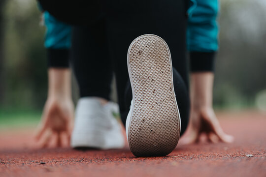 Runner's shoe is in focus as they prepare to start on a track. Foreground sole dominates the frame with a blurred background of the field.