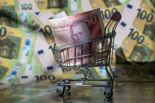 A 50 British pound note in a miniature supermarket shopping trolley with 100 euro notes in the background