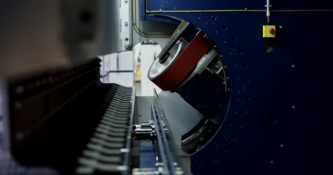 Automated metal beveling machine with sandpaper belt and emergency stop button in industrial factory workshop