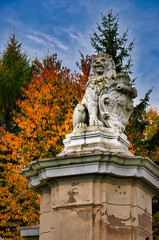 Obraz premium Stone Lion Statue On Historic Pillar With Heraldic Shield Amid Autumn Trees And Blue Sky. Lions Gate - Książański Landscape Park.
