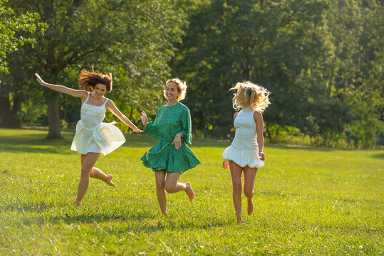 Women friends running barefoot through grass in summer on a sunny day