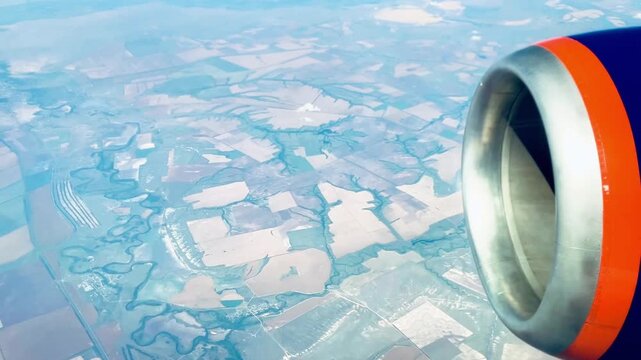 Airplane window view with jet engine flying above clouds and agricultural fields below. Scenic aerial countryside landscape, aviation and travel concept