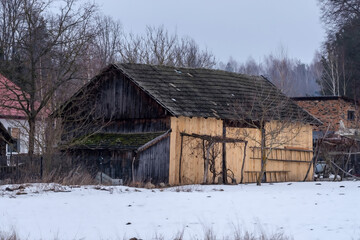 Stara, zabytkowa stodoła (częściowo odnowiona) z dachem pokrytym dach&oacute;wką betonową. Renowacja obejmuje świeży, drewniany segment frontowy, kontrastujący ze starym, ciemniejszym drewnem. 