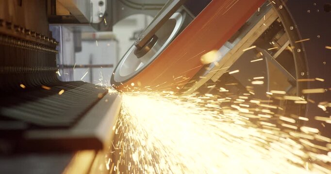 Industrial beveling machine grinding metal component with bright sparks flying in factory workshop