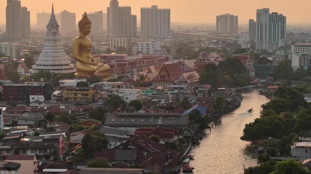 Aerial view Sunset light of the giant gold buddha in Wat Paknam Phasi Charoen Temple in Phasi Charoen district on Chao Phraya River with traditional boat, Bangkok, Thailand. Downtown City.