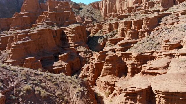 Aerial view captures majestic geological formations of erosion cliffs in arid Kyrgyzstan canyon. Cinematic wide angle ascending crane up camera movement showing volume via parallax effect.