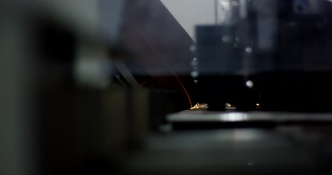Automated industrial beveling machine grinding metal part with bright orange sparks in a dark factory workshop