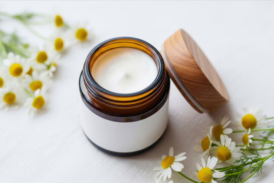 Mock-up product photo for a amber glass jar of a handmade herbal cream with a wooden lid beside it. The blank label for text and scattered chamomile flowers flowers with leaves for atmosphere