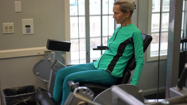 An elderly woman engages in a leg workout at the gym, using a machine to strengthen her legs and improve fitness levels.