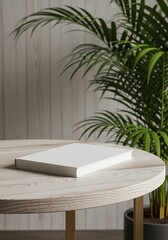 A white book rests on a round light wood table beside lush green plants