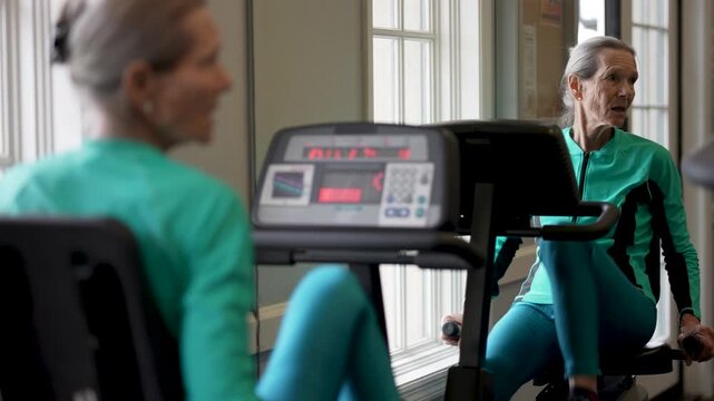 An elderly woman is working out on a gym machine focusing on fitness and health in a fitness room at a senior center.