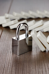 Naklejka premium Standing padlock after domino effect chain reaction. Security concept with lock firmly standing on the brown wooden table with pile of fallen domino tiles in background.