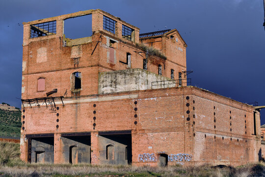 View of the old coal loading facility's weathered brick facade stands as a relic against the darkening sky, a testament to industrial history, Puertollano, Castile-La Mancha, Spain.