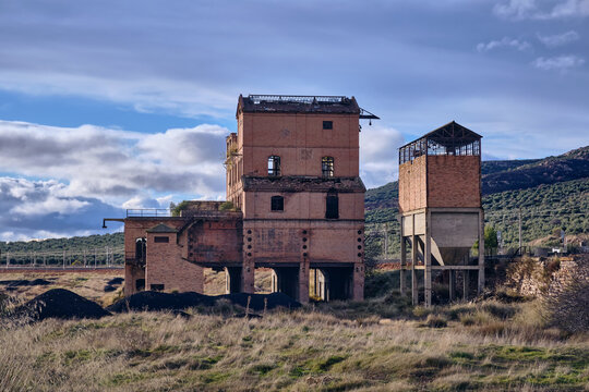 View of an old coal loading facility with decaying brickwork under a cloudy sky, a stark contrast to the dry landscape, Puertollano, Castile-La Mancha, Spain.