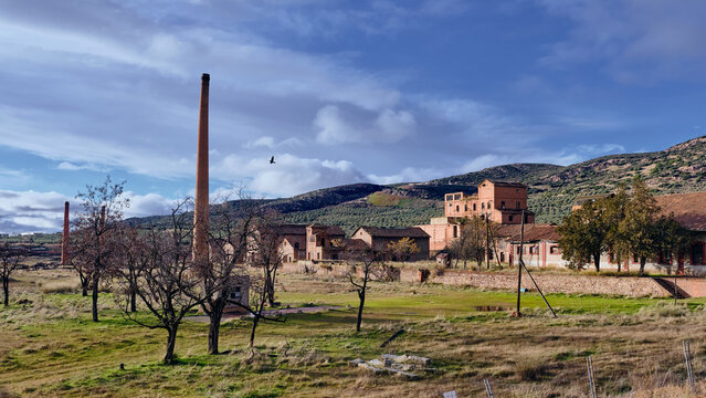 View of the abandoned, old coal loading facility with its brick structures and tall chimney under a cloudy sky, Puertollano, Castile-La Mancha, Spain.