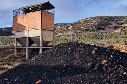 View of the stark contrast between the dark coal pile and a weathered brick structure against the hilly backdrop, Puertollano, Castile-La Mancha, Spain.