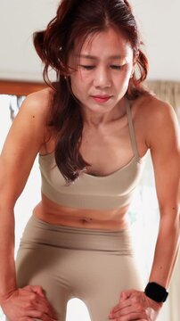 Focused young Asian woman performing Nauli Kriya or abdominal massage yoga pose at home. Advanced yoga practice and wellness concept shows intense core muscle control and physical fitness in portrait
