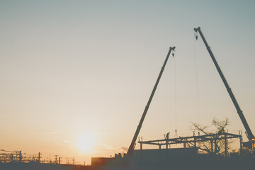 Fototapeta premium Silhouette of construction cranes, workers, and an overhead railway at sunset.