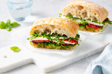 Ciabatta sandwich with mozzarella, tomatoes, pesto sauce and fresh basil on marble serving board....