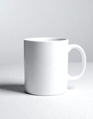 Obraz premium A plain white ceramic mug sits angled on a white surface with a simple white backdrop, softly shadowed