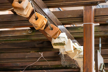 several square-shaped, tan-colored floats or weights hanging from a wire underneath a weathered wooden pier or structure. © Andrey