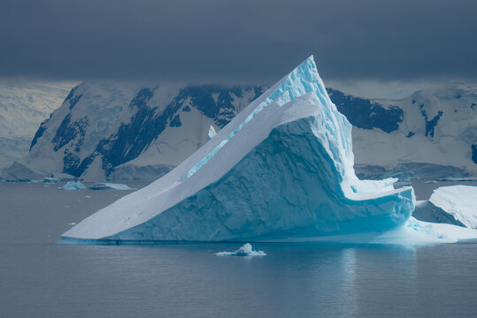 View of a colossal, angular iceberg, a frozen titan, rises from the frigid waters under a brooding sky, Portal Point, Graham Land, Antarctica.