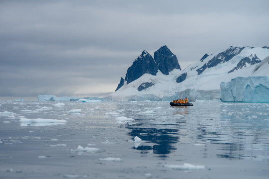 View of a vibrant yellow zodiac boat navigating the frigid, icy waters beneath snow-capped mountains and glaciers, Portal Point, Antarctica.