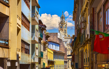 Fototapeta premium Porto, Portugal. Cosy street with traditional colorful houses of old town. View at high medieval tower clock. Sunny summer day. Residential porto city district beautiful antique portugal buildings.