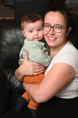 young child in his mother's arms, facing a black sofa