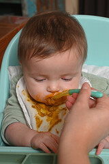 young child in a chair eating clumsily with a spoon