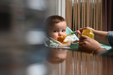 young child in a chair eating clumsily with a spoon, with a blurry reflection on the side