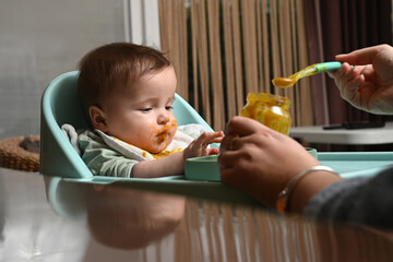 young child in a chair eating clumsily with a spoon