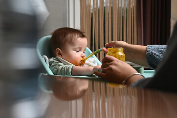 young child in a chair eating clumsily with a spoon, with a blurry reflection on the side