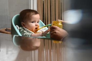 young child in a chair eating clumsily with a spoon, with a blurry reflection on the side