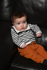 close-up of a young child wearing a sailor shirt sitting on a black sofa
