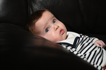 close-up of a young child wearing a sailor shirt sitting on a black sofa