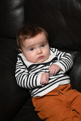 close-up of a young child wearing a sailor shirt sitting on a black sofa