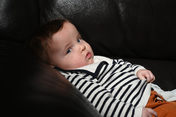 close-up of a young child wearing a sailor shirt sitting on a black sofa