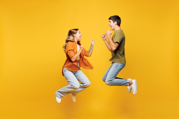Full body side view young couple friends family man woman wear casual clothes together jump high do winner gesture clench fist isolated on pastel plain light yellow color background studio portrait © ViDi Studio