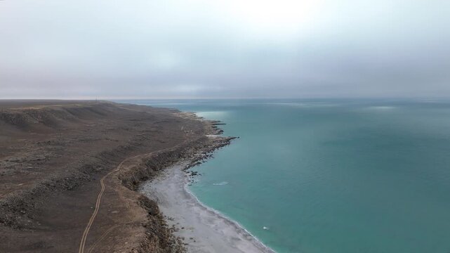 Scenic hidden white sand beach on the Caspian Sea coast in Mangystau, Aktau, Kazakhstan. Turquoise blue water, brown rocky cliffs, light fog and no people create a sense of isolation and exclusivity