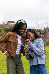 African American teenage girls standing on grass pointing at tablet, holding coiled earphones