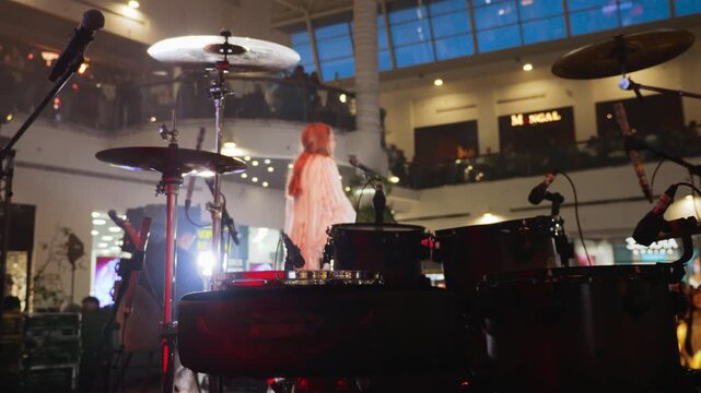 Female singer performing a live vocal set in a spacious shopping mall atrium. The stage setup includes a professional drum kit , creating a unique solo performance atmosphere. 
