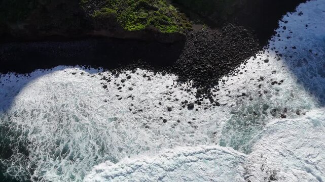 Aerial view of ocean waves crashing onto rocky shore with foam and splashes, showcasing the dynamic interaction between water and land in a coastal environment. Scenic sea landscape. Close up shot