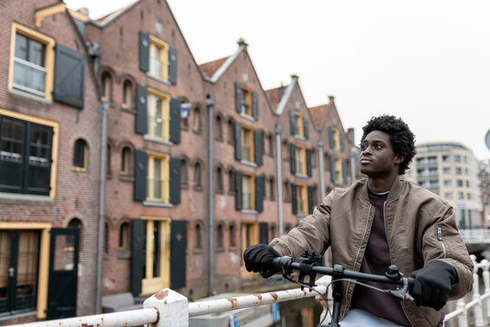 Young black man riding bicycle in a scenic dutch city by canal houses, representing urban diversity and inclusion