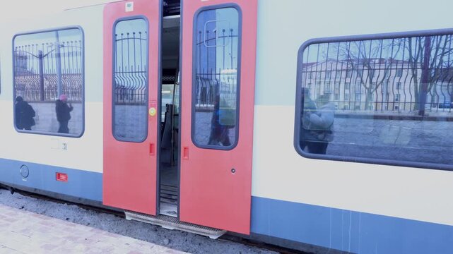 A train with red doors is stopped at a station, allowing passengers to board and disembark.
