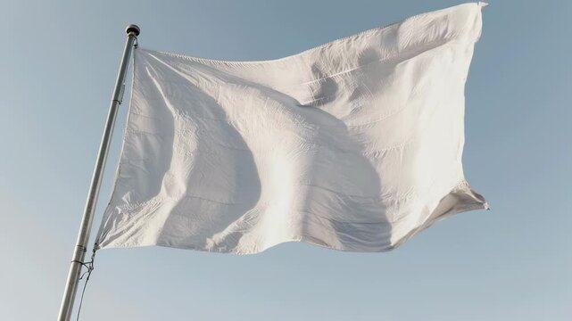 A white flag billows in the wind against a clear sky