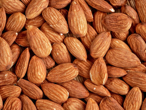 A close-up shot shows a pile of whole, raw almonds. The almonds are oval-shaped with brown skin and appear to be dry and roasted.