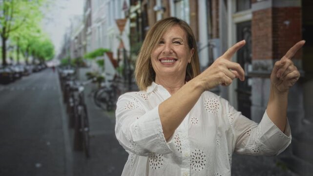 Woman smiling and pointing fingers toward unseen direction on sunlit urban street; guidance cheerfulness.