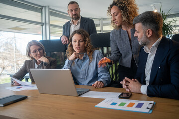 Obraz premium Businesswoman reviewing report on her laptop while discussing business growth with coworkers in meeting 